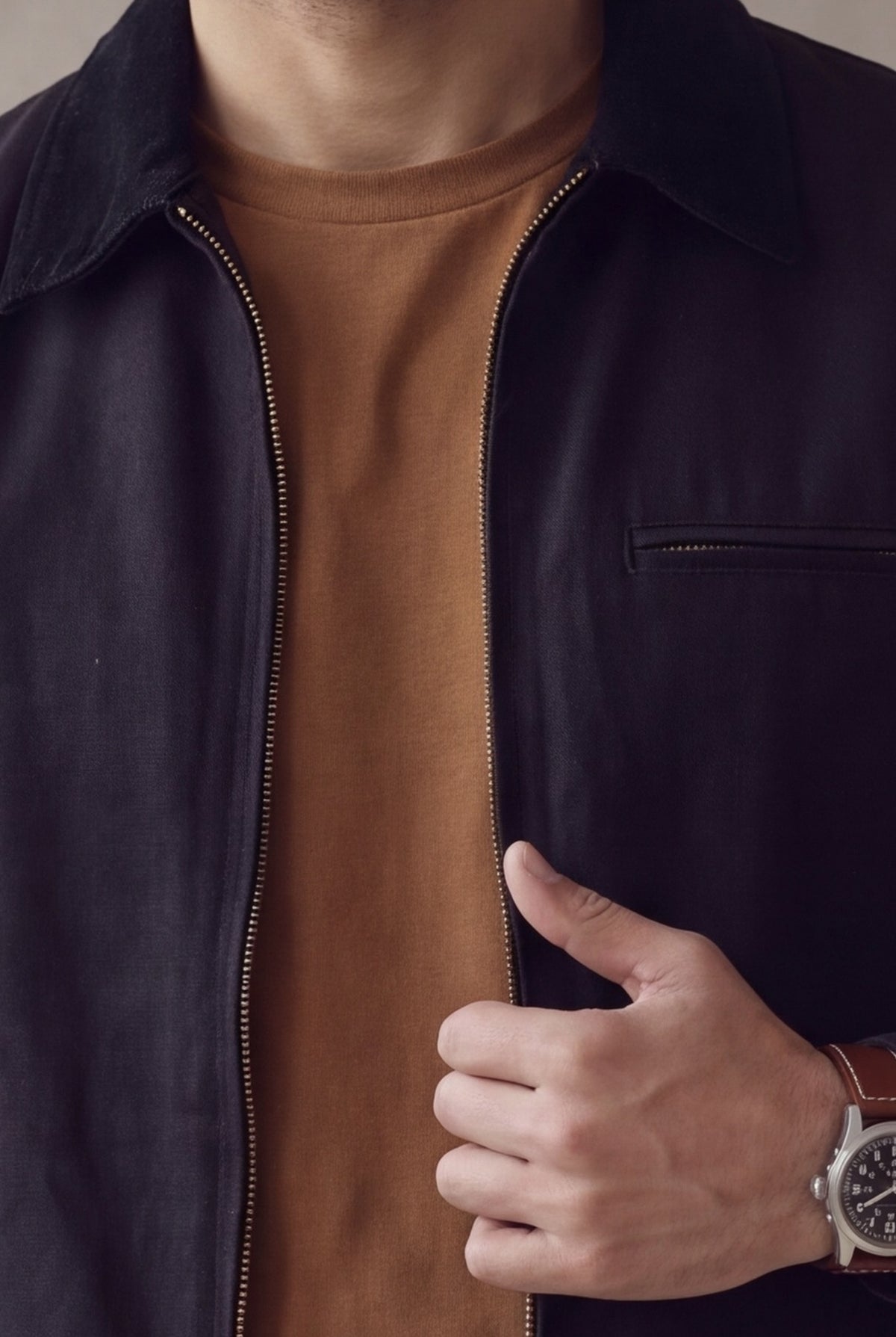 Detalle de la chaqueta Detroit negra para hombre de Luck & Load: cuello de pana, cierre de laton, bolsillo de cremallera y reloj, sobre camiseta cafe.