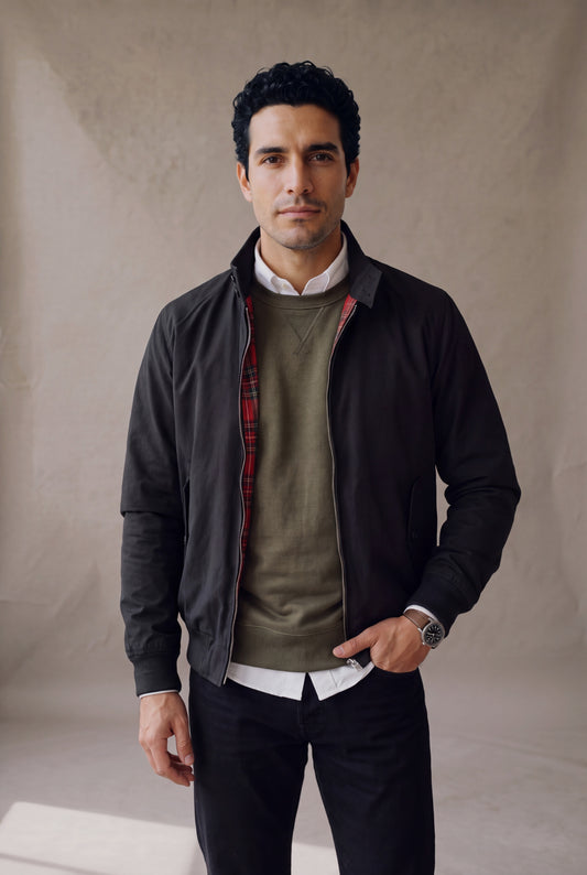 Medio cuerpo de la chaqueta Harrington negra de Luck & Load en capas sobre buzo verde oliva y camisa blanca.