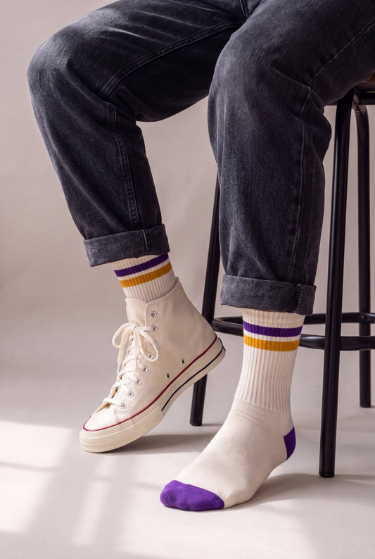 Medias largas crema con franja morada y dorada, en hombre sentado con jean negro y Converse crema, caña completa a la vista