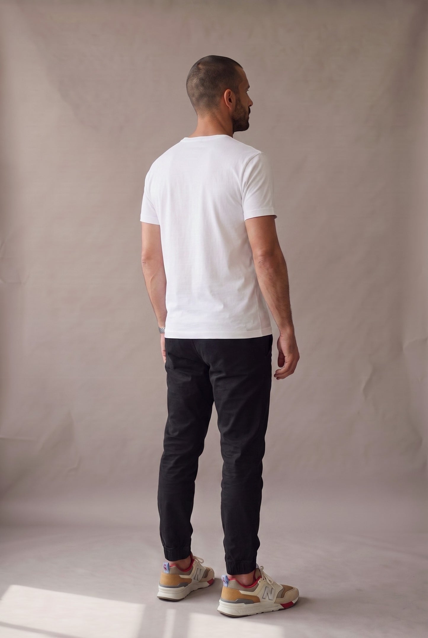 Vista de espalda de la camiseta blanca de cuello redondo con bolsillo, jogger negro y tenis claros