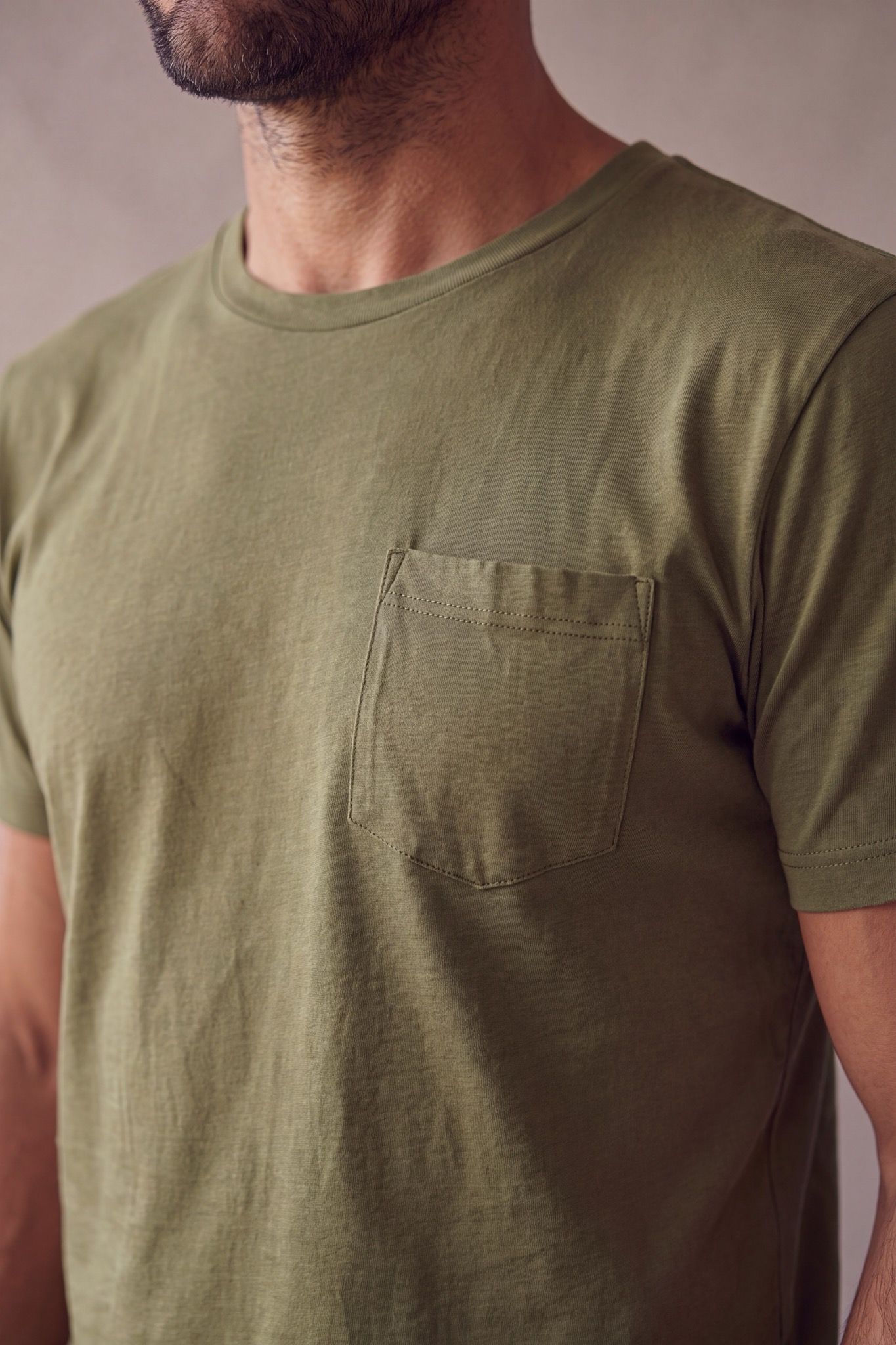 Detalle del bolsillo de pecho pentagonal, el cuello y la tela de la camiseta verde militar de cuello redondo en algodon peruano.