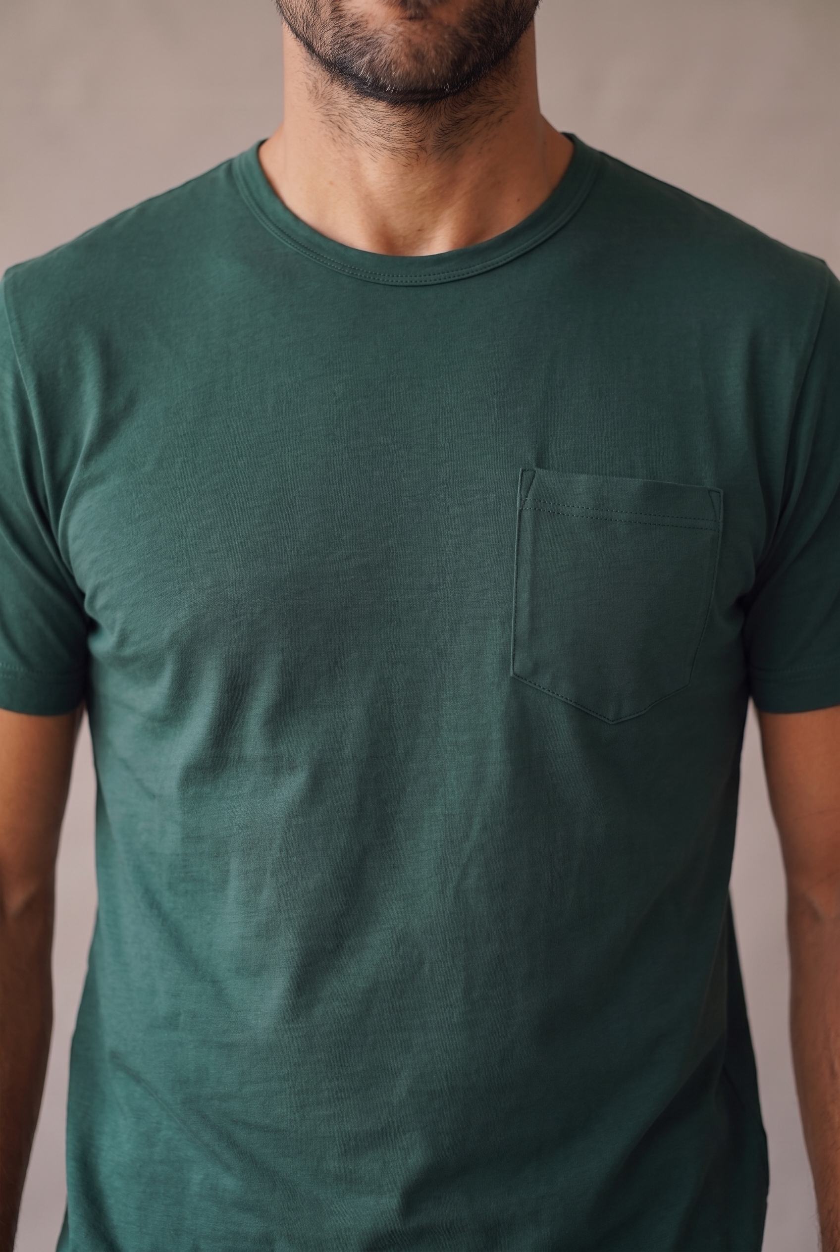 Detalle del bolsillo de pecho pentagonal, el cuello y la tela de la camiseta verde pino de cuello redondo en algodon peruano.