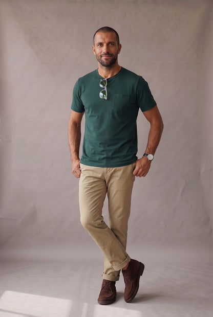 Hombre de frente con camiseta verde pino de cuello redondo con bolsillo en algodon peruano, foto de catalogo en estudio.
