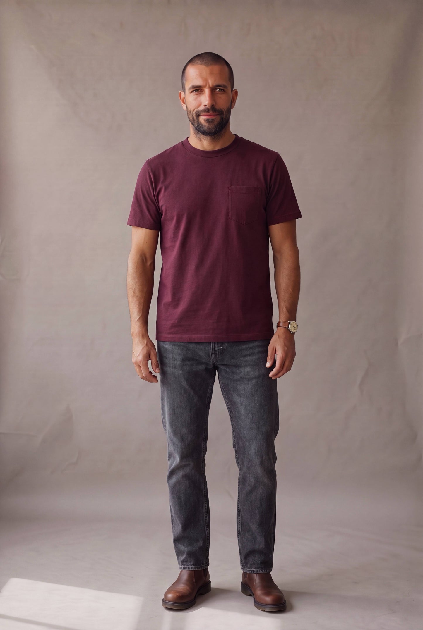 Hombre de frente vistiendo la camiseta de cuello redondo vinotinto con bolsillo de Luck and Load, con jeans gris oscuro; foto de catalogo en estudio.