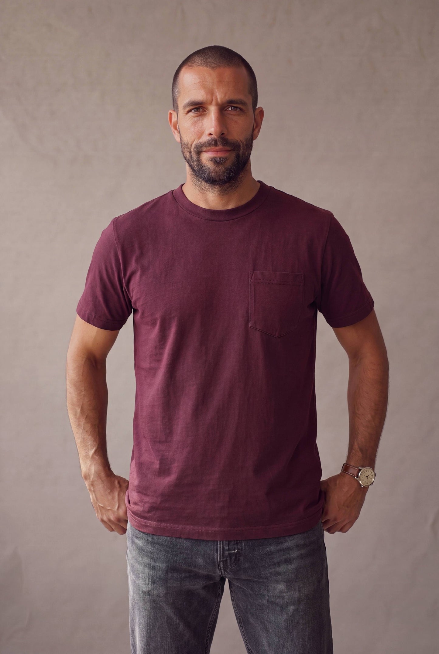Plano medio de hombre con la camiseta de cuello redondo vinotinto con bolsillo de Luck and Load y jeans gris oscuro; foto de catalogo en estudio.