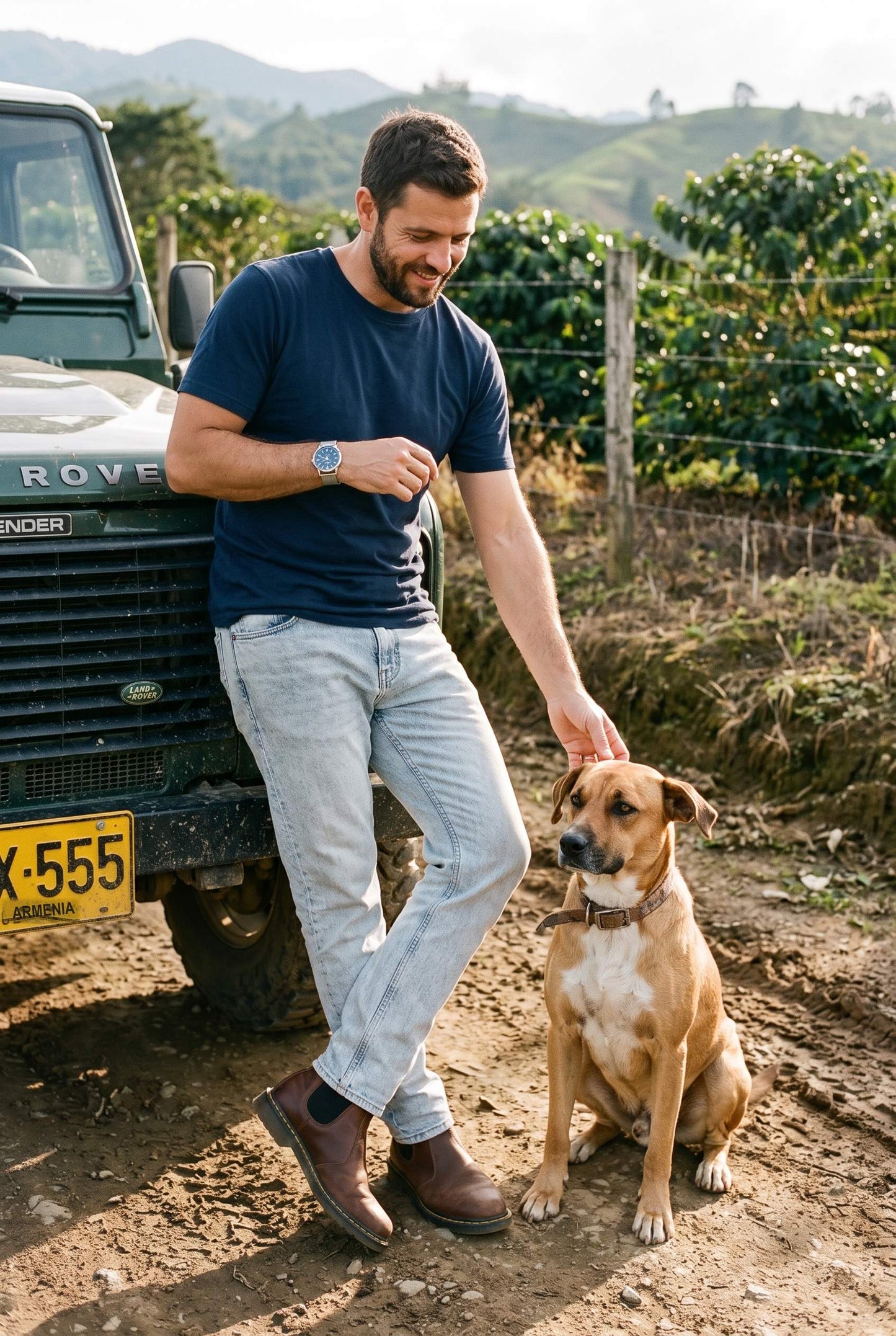 Hombre con camiseta azul marino de cuello redondo de Luck & Load junto a un Land Rover Defender y un perro criollo en una trocha de finca cafetera en Colombia.