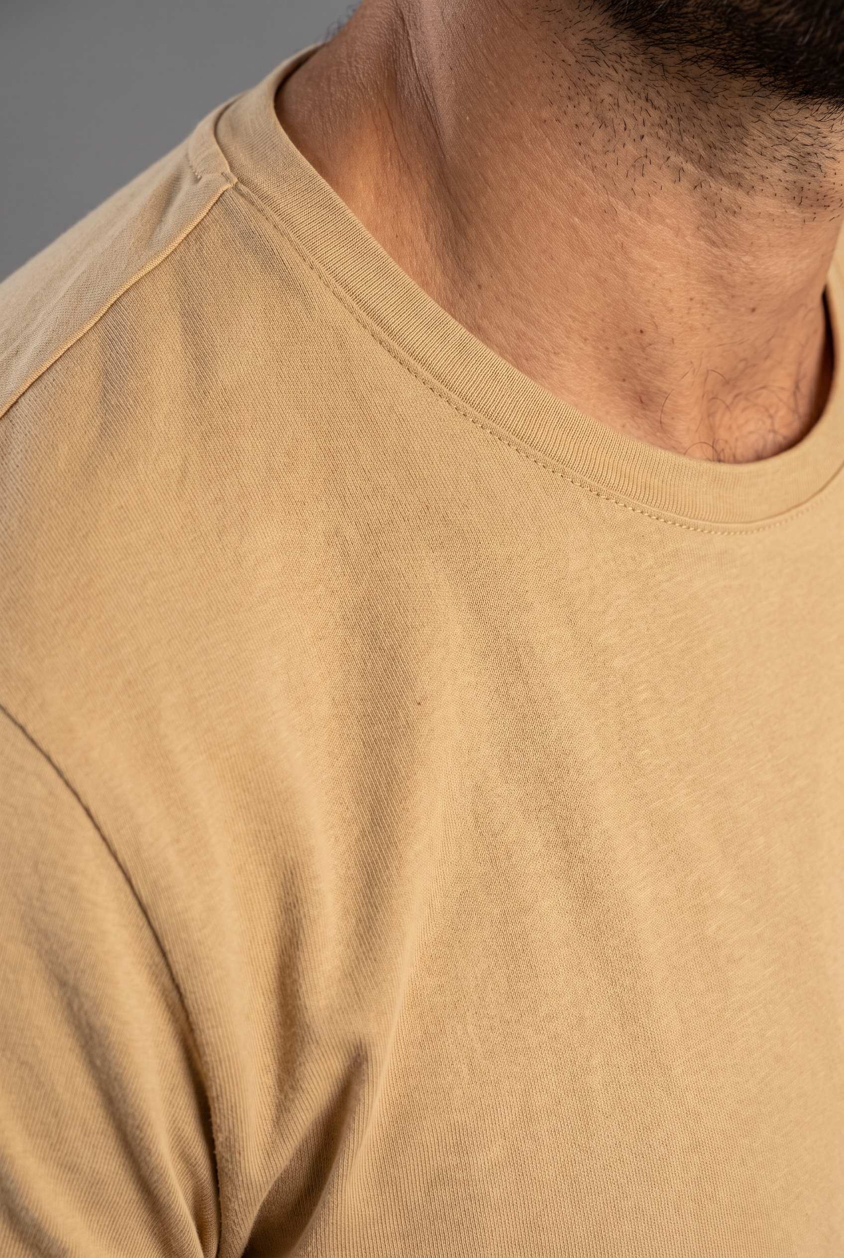 Detalle del cuello redondo y la costura de hombro de la camiseta beige de Luck & Load en algodón mate