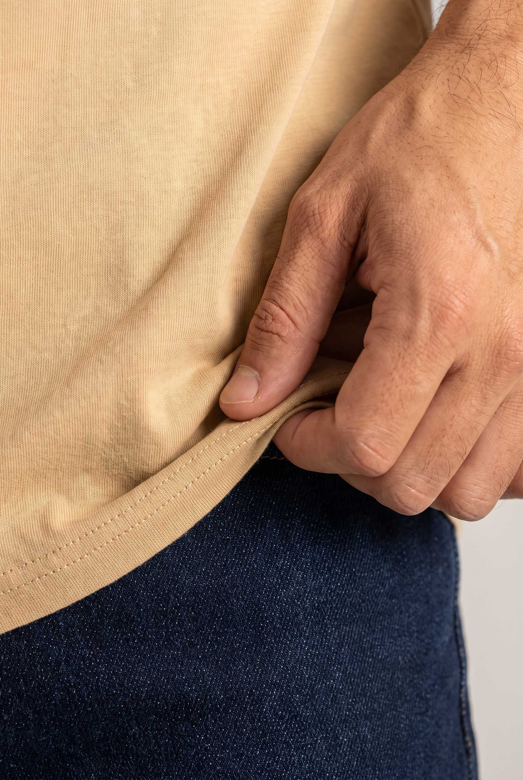 Primer plano del algodón de la camiseta beige de cuello redondo de Luck & Load, con la tela estirada entre las manos sobre el jean índigo