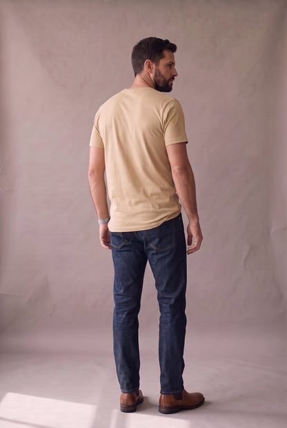 Vista de espalda de la camiseta beige de cuello redondo de Luck & Load, con el largo y la caída del algodón sobre un hombre de pie