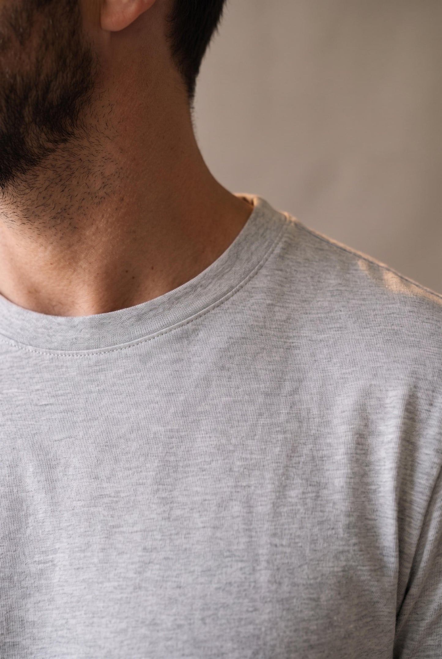 Detalle del cuello redondo de la camiseta gris de hombre, ribete plano y limpio visto de perfil
