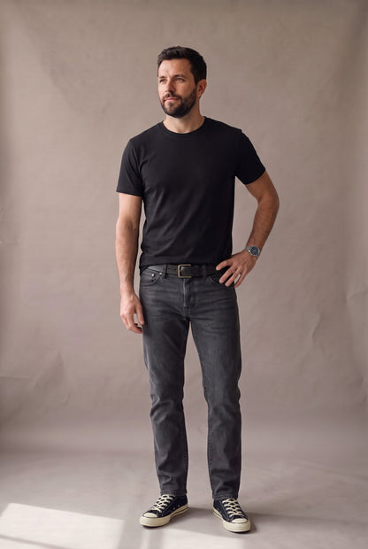 Hombre de pie con camiseta negra de cuello redondo sin bolsillo de Luck & Load, con jean gris grafito y tenis de lona negros.