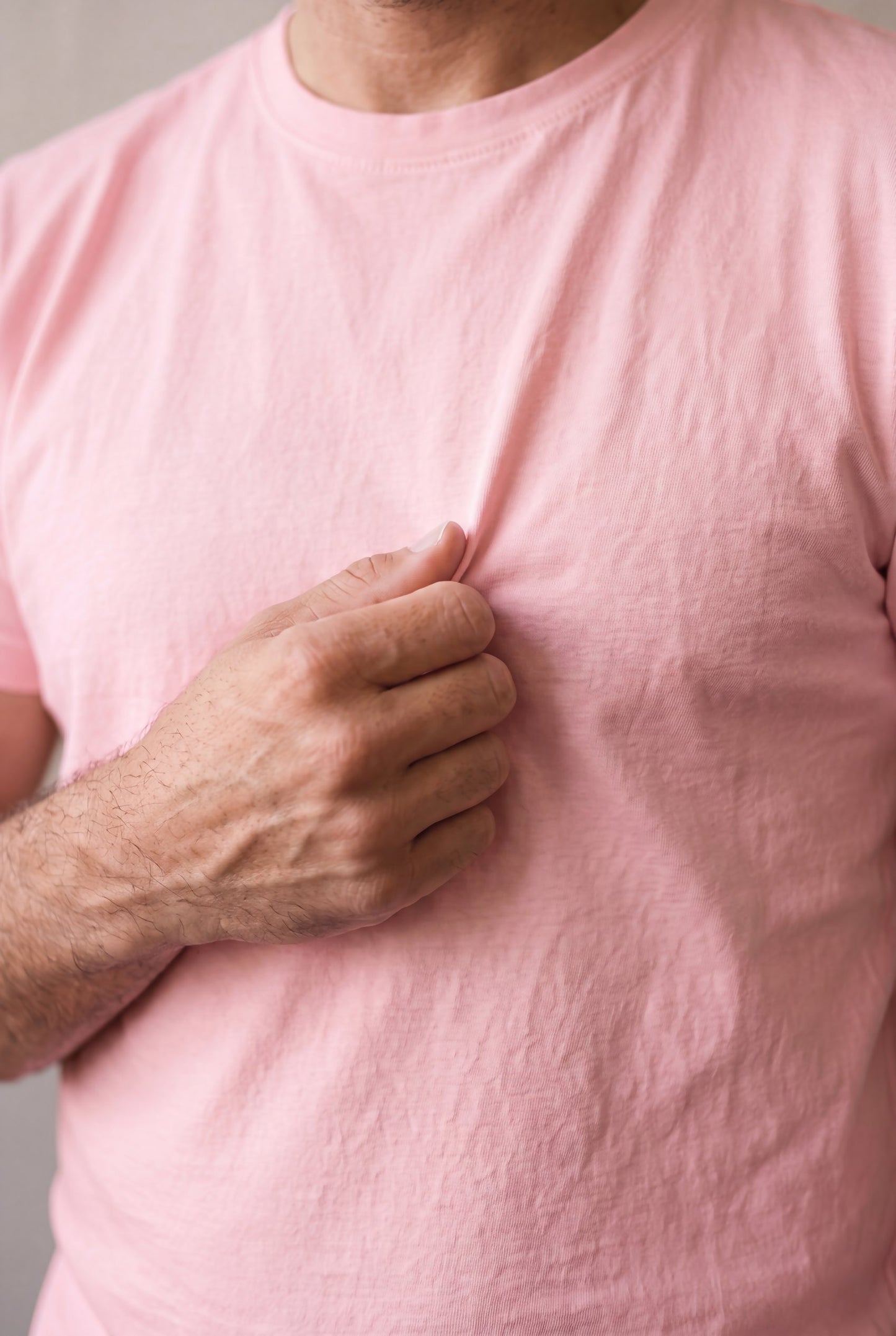 Primer plano del tejido de algodón peruano de la camiseta rosa palo de Luck & Load sostenido entre los dedos.