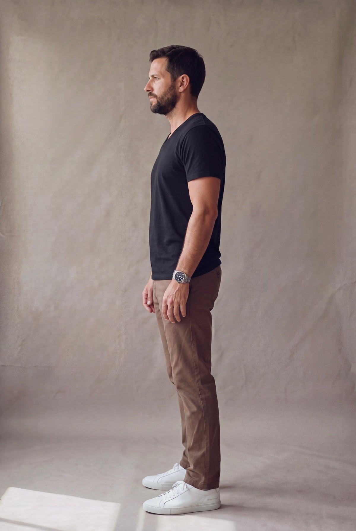 Vista lateral de la camiseta cuello en V negra Luck and Load con pantalon cafe y tenis blancos