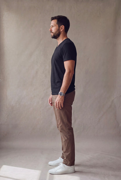 Vista lateral de la camiseta cuello en V negra Luck and Load con pantalon cafe y tenis blancos