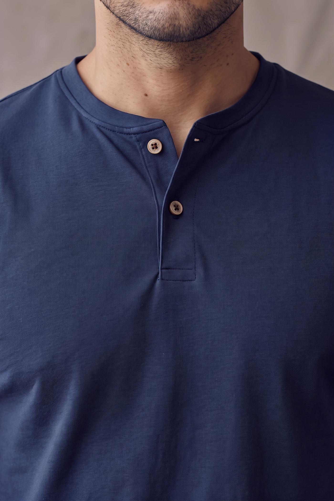 Detalle de la cartera de la camiseta azul marino Luck & Load, con pespunte tonal y dos botones de corozo caramelo