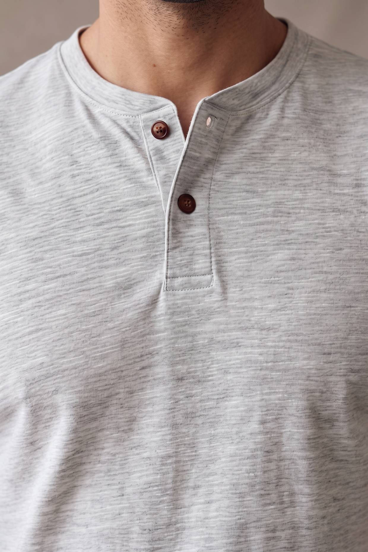 Detalle de la cartera de la camiseta gris jaspe Luck & Load, con pespunte tonal y dos botones de corozo caramelo