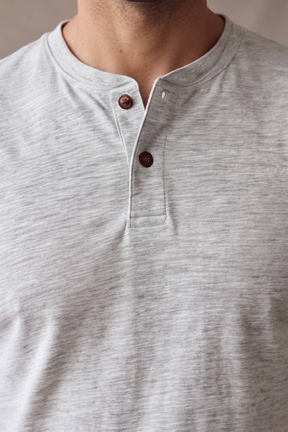 Detalle de la cartera de la camiseta gris jaspe Luck & Load, con pespunte tonal y dos botones de corozo caramelo