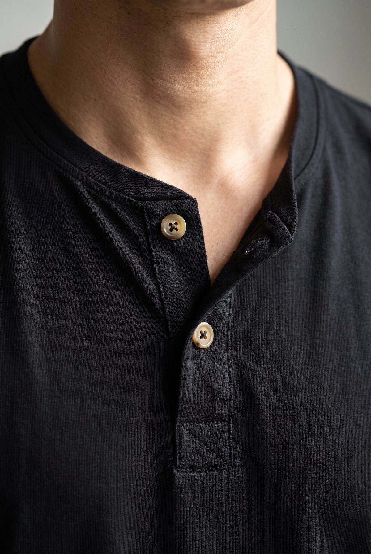 Detalle de la cartera de la camiseta negra Luck & Load, con pespunte tonal y dos botones de corozo claro