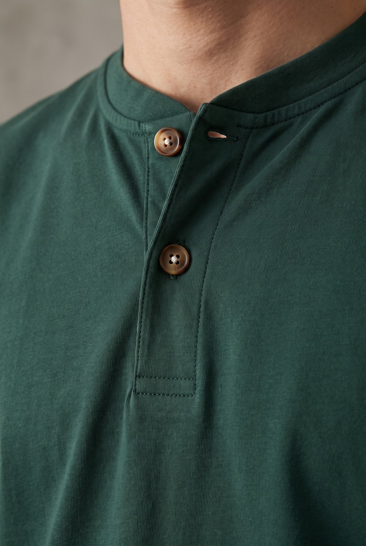 Detalle de la cartera de la camiseta verde pino Luck & Load, con pespunte tonal y dos botones de corozo claro