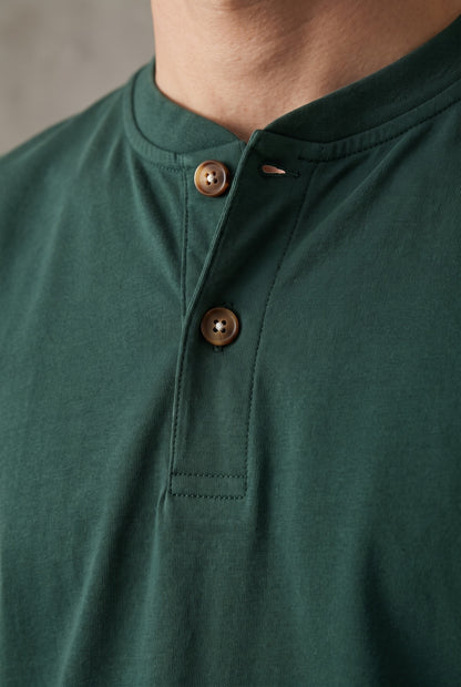 Detalle de la cartera de la camiseta verde pino Luck & Load, con pespunte tonal y dos botones de corozo claro