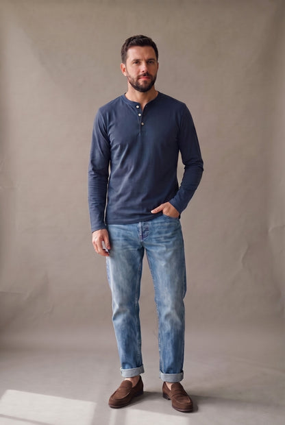 Hombre de frente con camiseta henley manga larga azul marino de tres botones, jean y mocasines café.