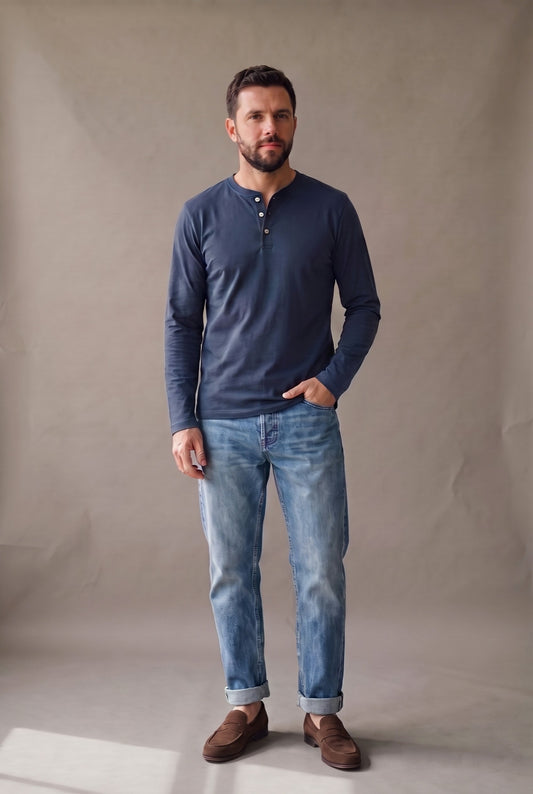 Hombre de frente con camiseta henley manga larga negra de tres botones y jean gris.