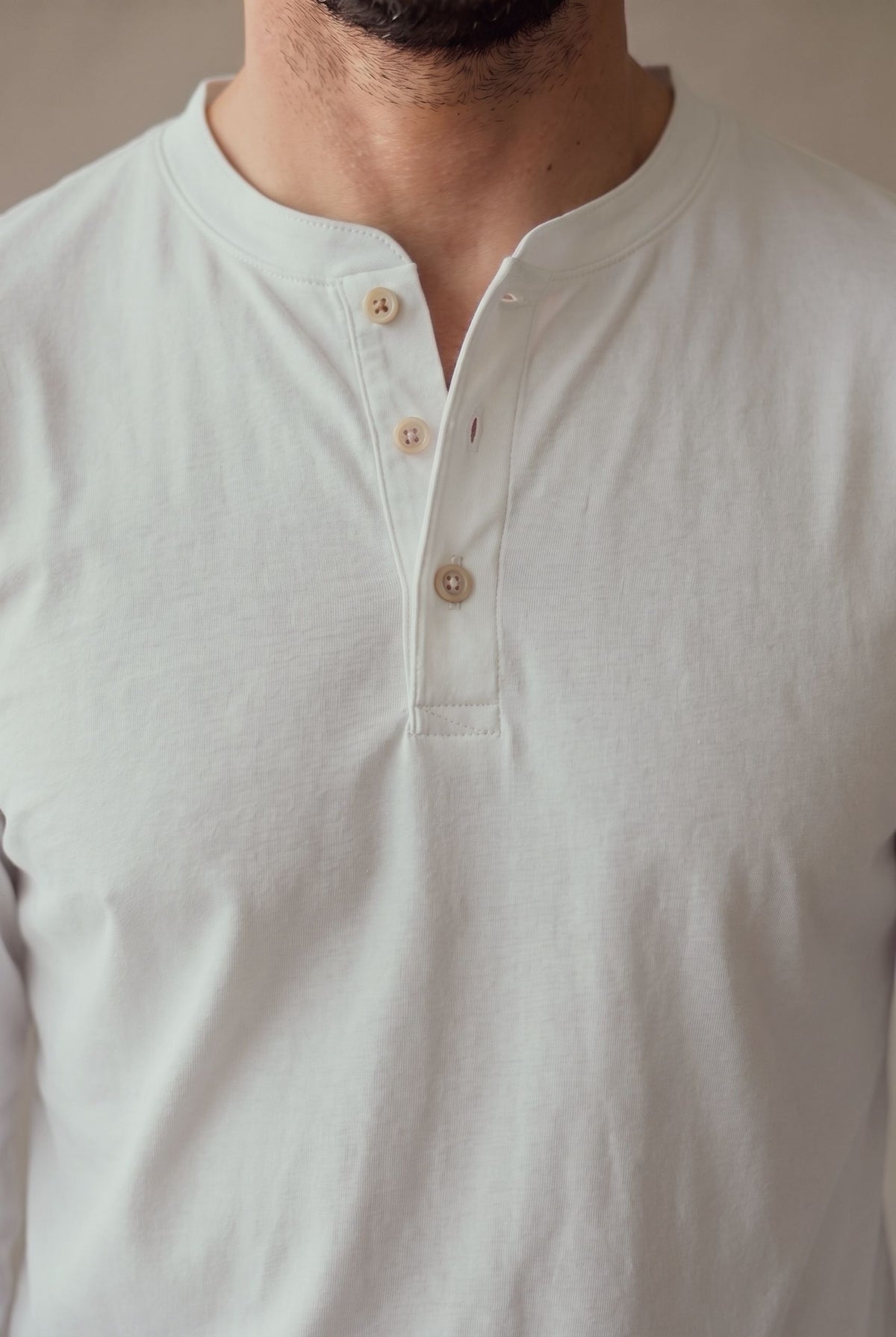 Detalle de la cartera de tres botones de corozo y el cuello de la camiseta henley blanca.