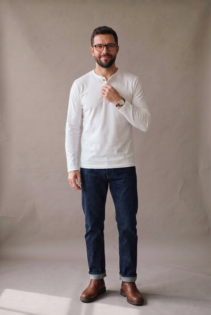 Hombre de frente con camiseta henley manga larga blanca de tres botones, jean índigo y botas café.