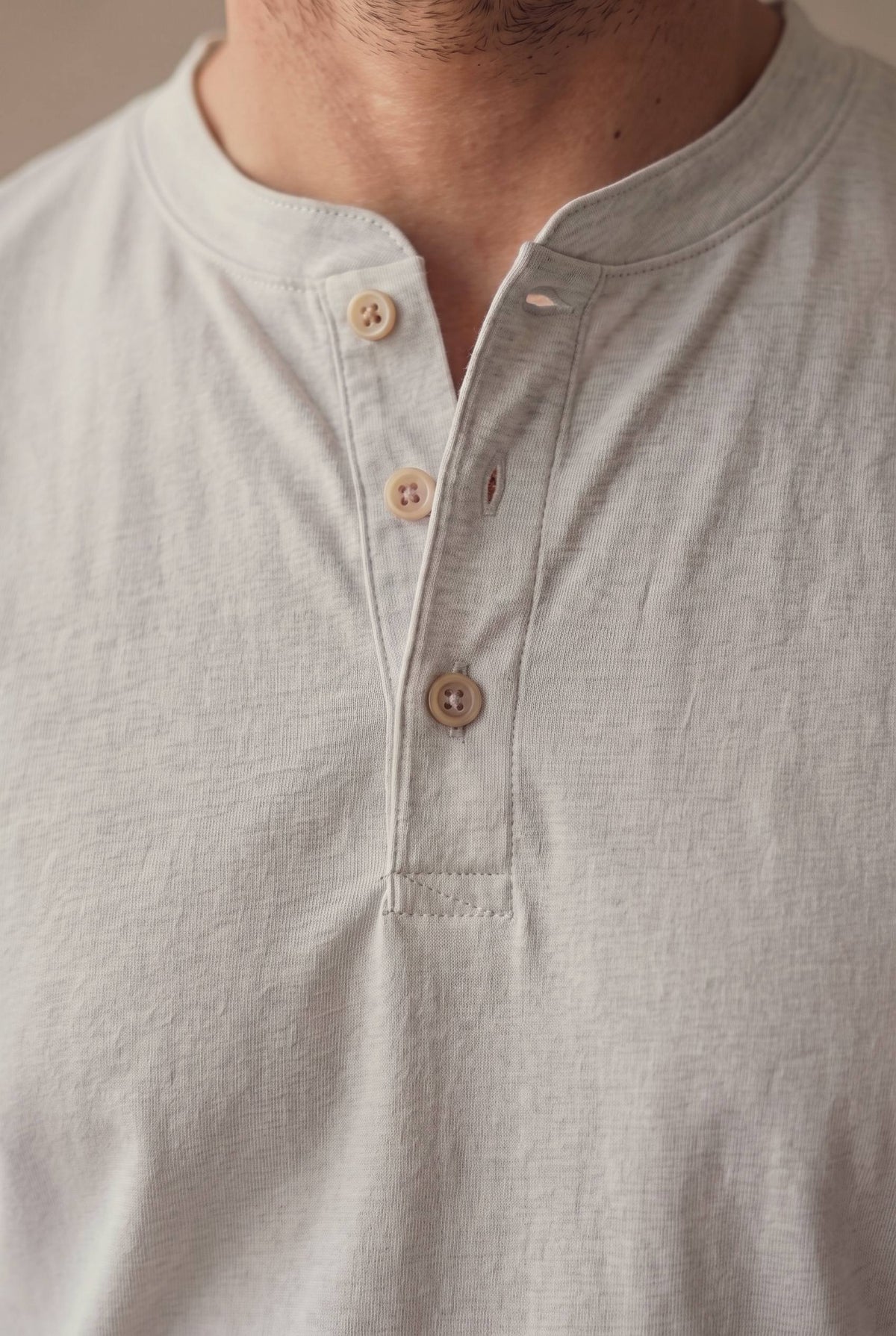 Detalle del cuello de banda, la cartera y los tres botones de corozo crema de la camiseta henley gris jaspe.