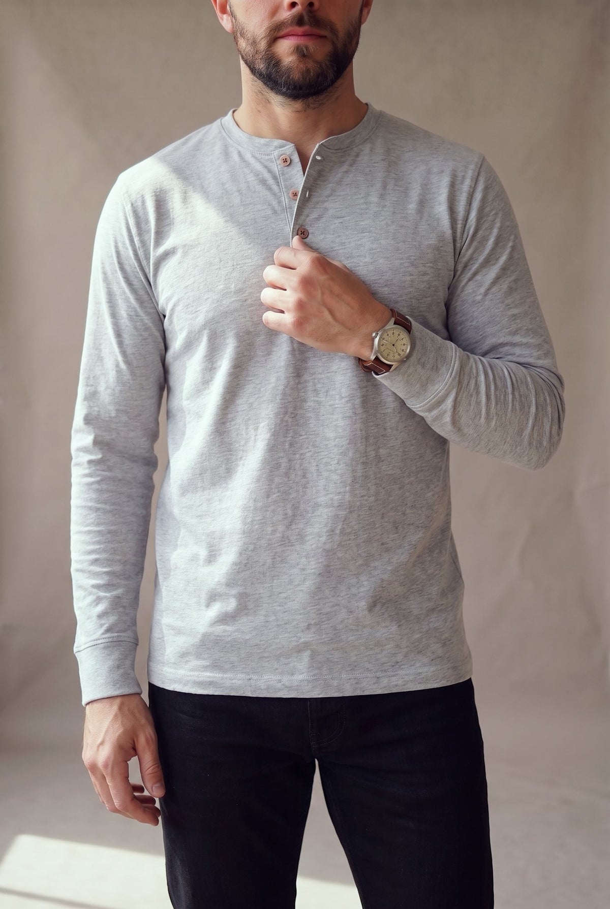 Medio cuerpo de la camiseta henley gris jaspe con la cartera de tres botones de corozo crema.