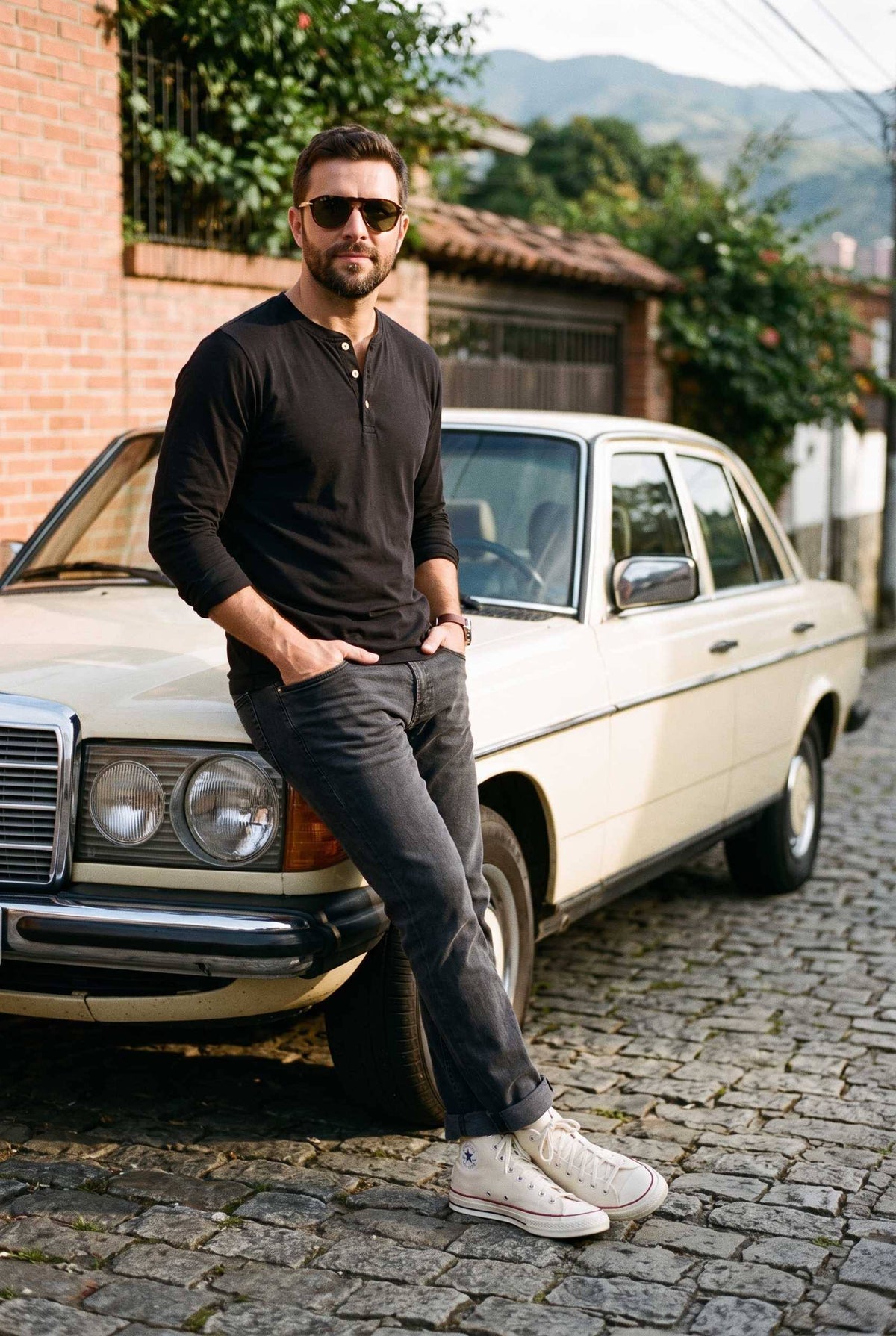 Hombre con la camiseta henley negra junto a un auto clásico en un look urbano de fin de semana.