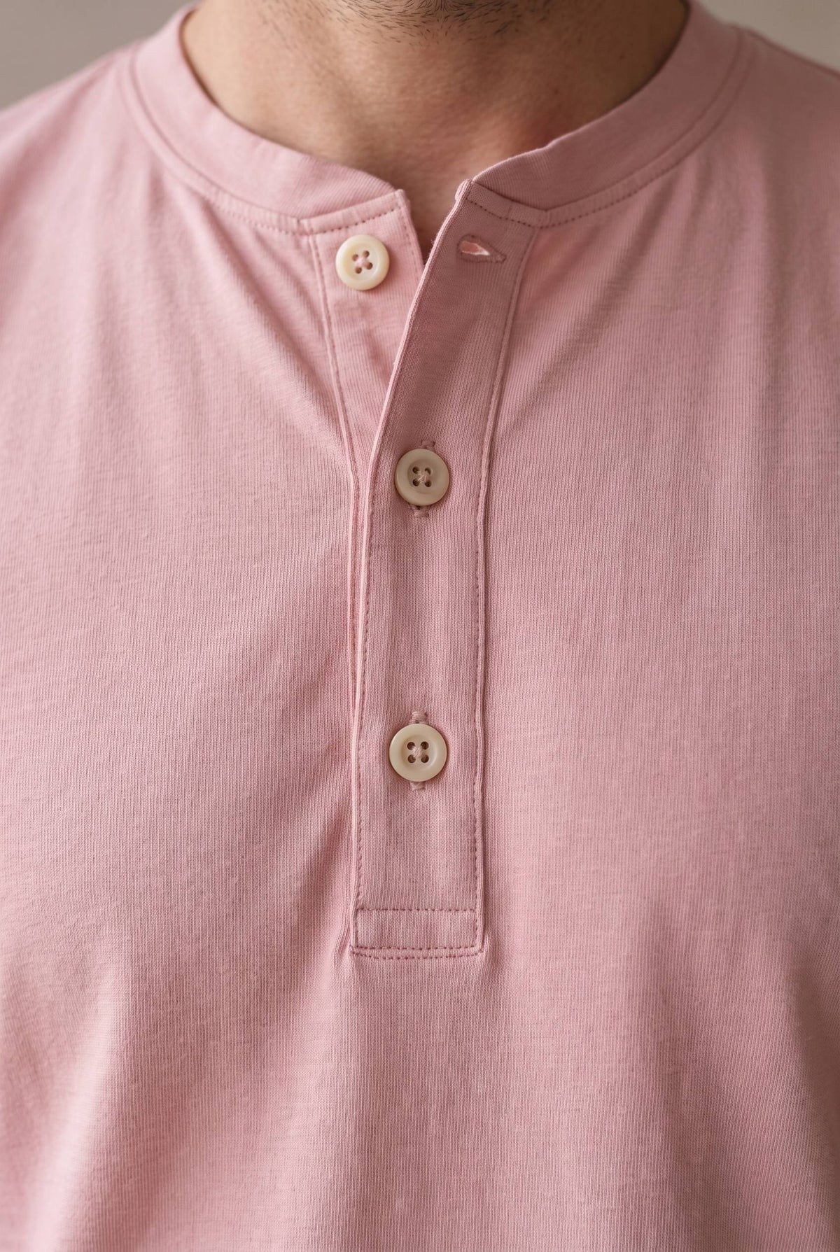 Detalle del cuello de banda, la cartera y los tres botones de corozo crema de la camiseta henley rosado palo de rosa.