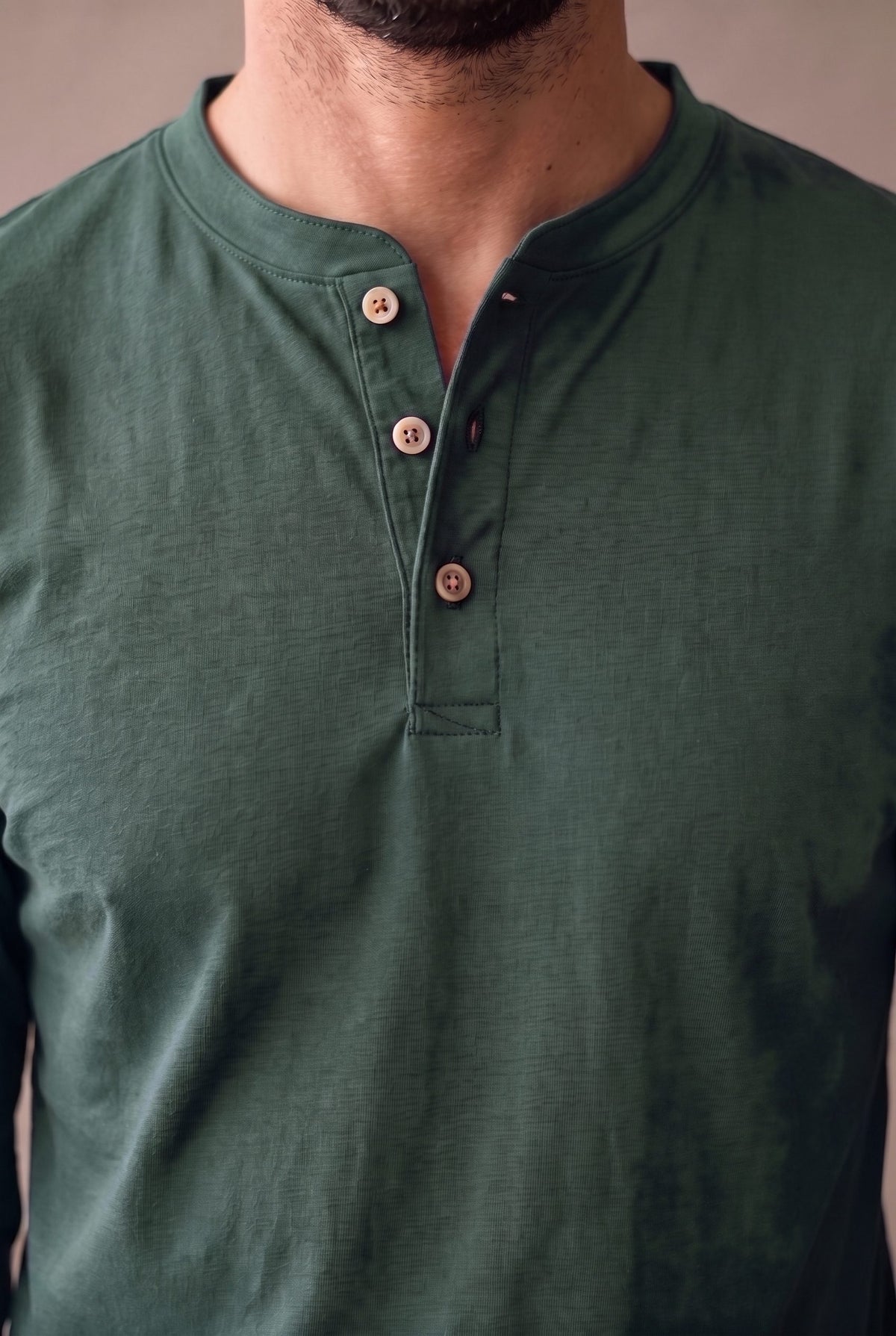 Detalle de la cartera con tres botones de corozo y el cuello de banda de la camiseta henley verde pino