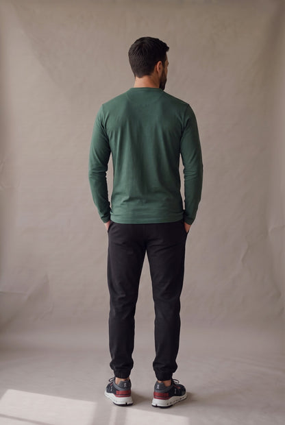 Vista de espalda de la camiseta henley verde pino con panel limpio, jogger negro y tenis On