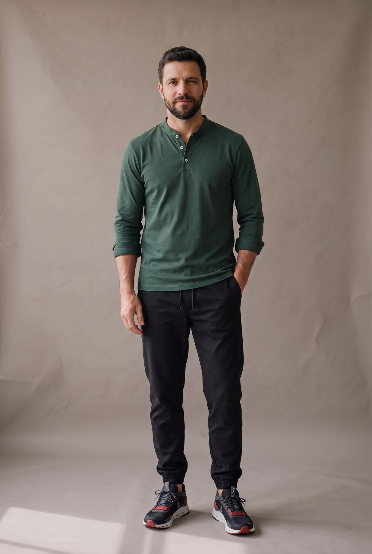 Hombre de frente con la camiseta henley verde pino de tres botones, jogger negro y tenis On, en look sport