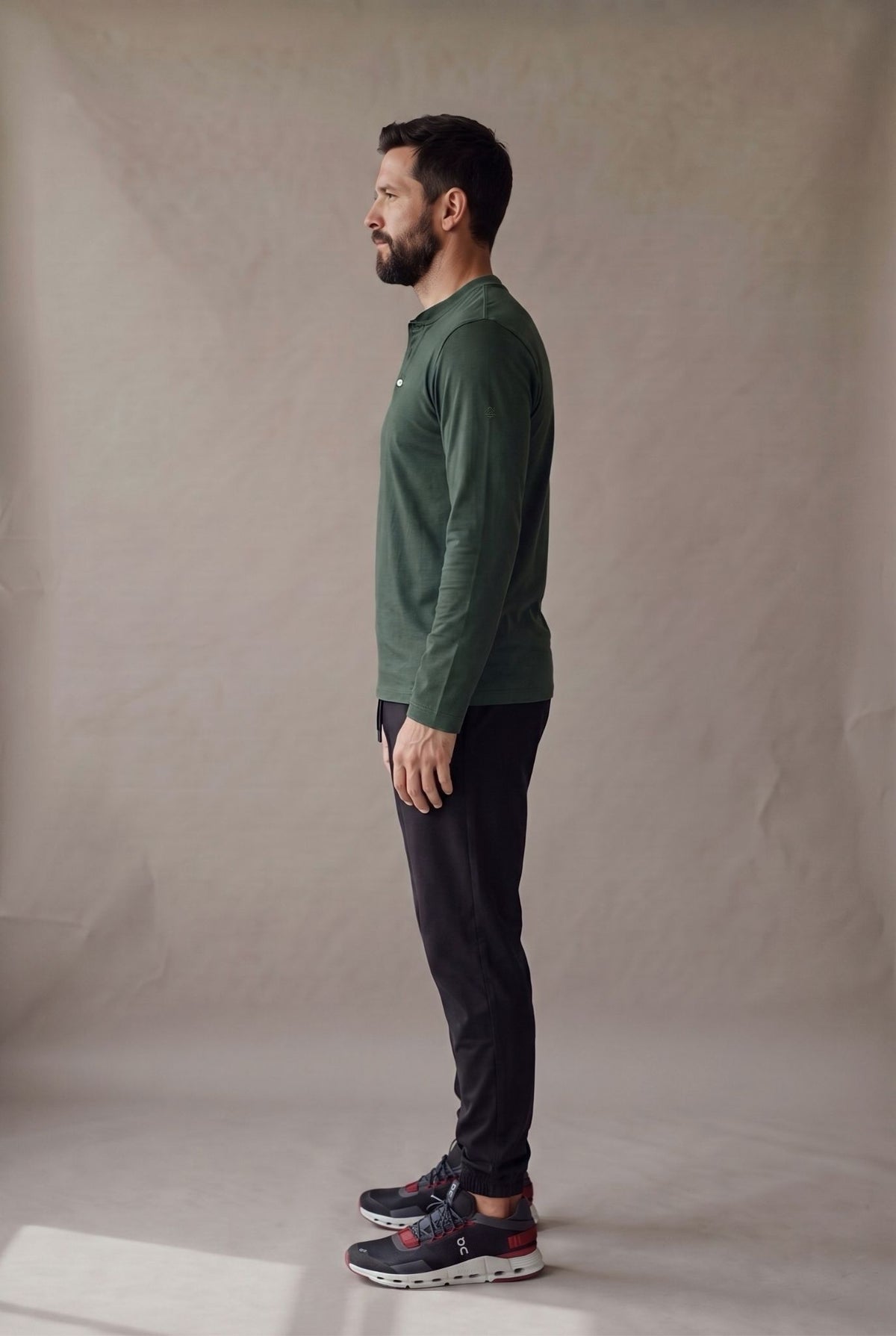 Vista lateral de la camiseta henley verde pino sobre jogger negro, con la caida limpia y el puno liso