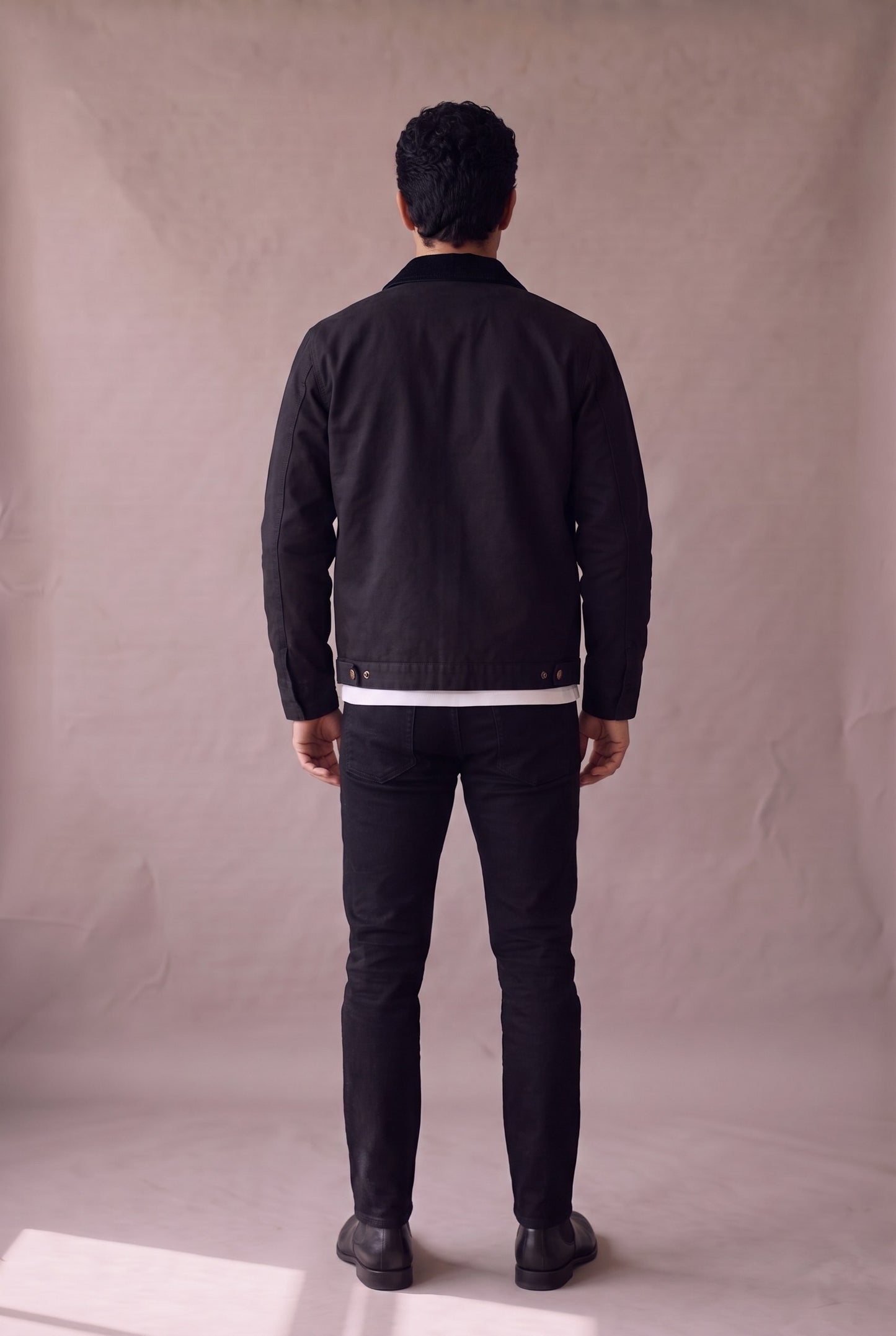 Chaqueta Detroit negra de Luck and Load, vista de espalda; canesu trasero y broches de ajuste, sobre jean negro y botin Chelsea negro. Colombia
