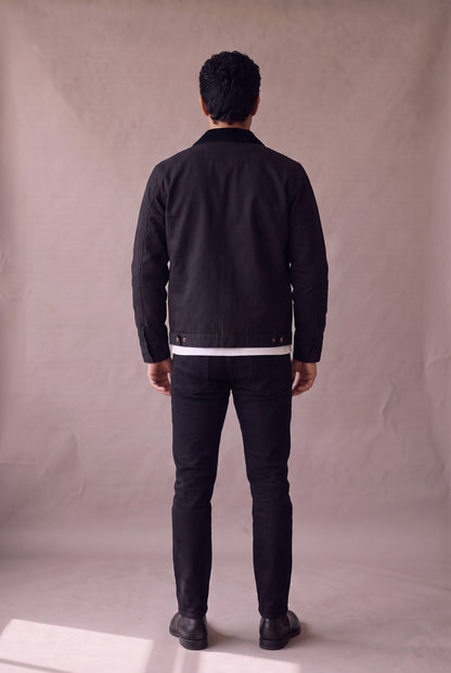 Chaqueta Detroit negra de Luck and Load, vista de espalda; canesu trasero y broches de ajuste, sobre jean negro y botin Chelsea negro. Colombia