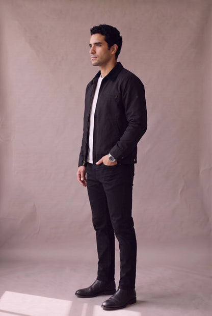 Chaqueta Detroit negra de cuello de pana de Luck and Load, vista de tres cuartos de pie; hombre con camiseta blanca, jean negro recto y botin Chelsea negro. Colombia