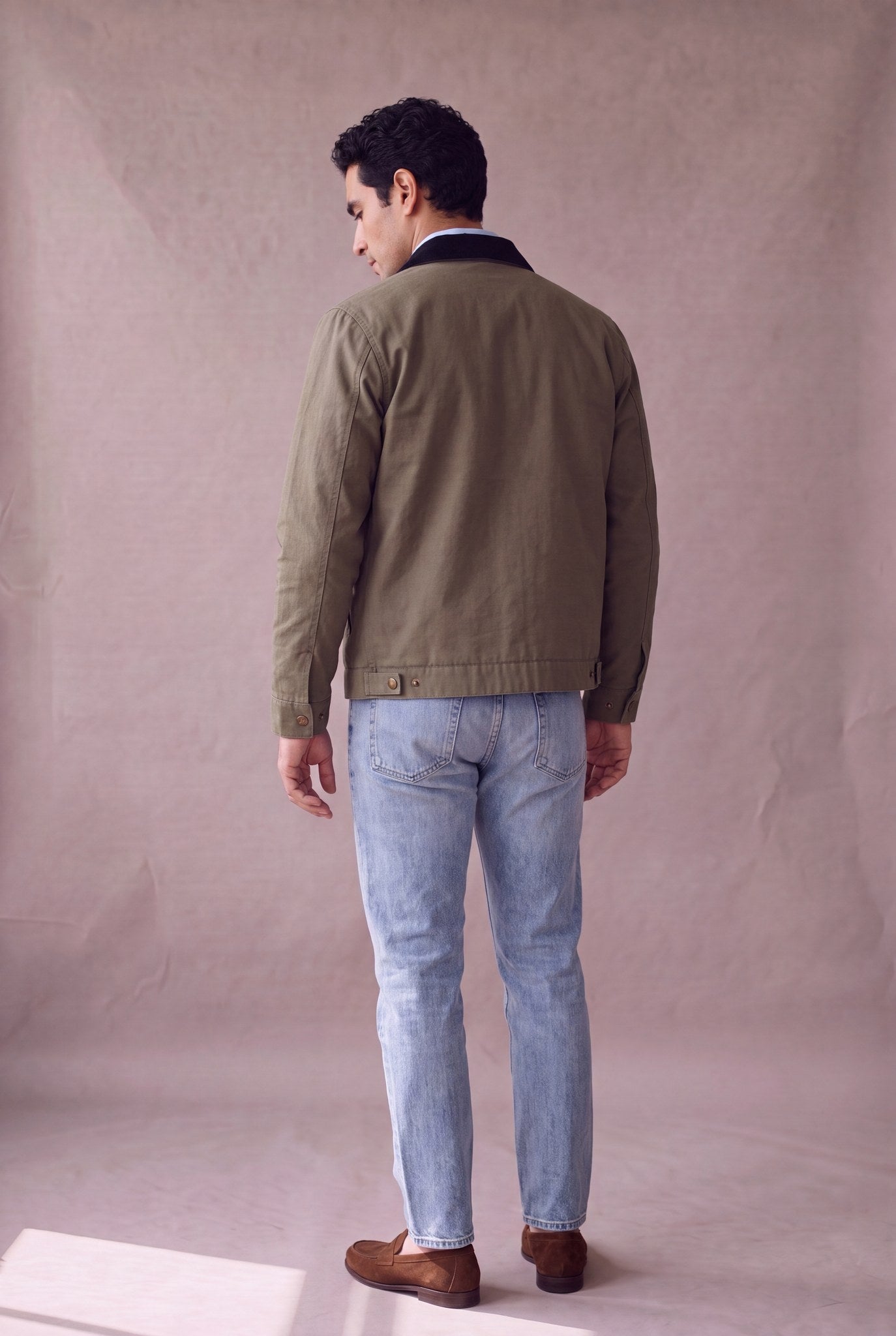 Chaqueta Detroit color verde oliva militar de Luck and Load con cuello de pana negro, vista de espalda; canesu trasero y broches, sobre jean claro y mocasin de gamuza. Colombia