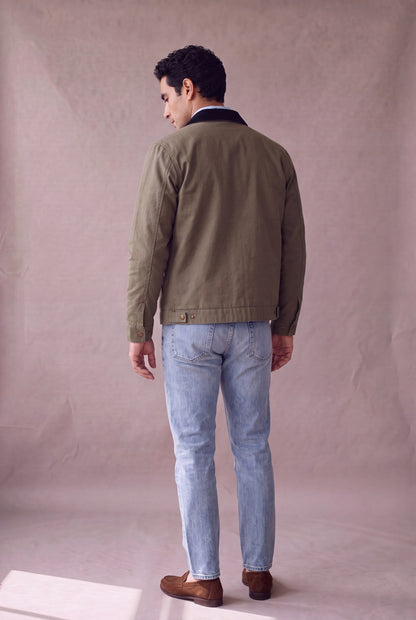 Chaqueta Detroit color verde oliva militar de Luck and Load con cuello de pana negro, vista de espalda; canesu trasero y broches, sobre jean claro y mocasin de gamuza. Colombia