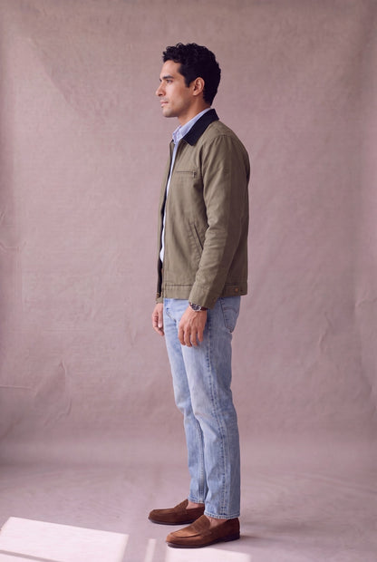 Chaqueta Detroit color verde oliva militar de Luck and Load con cuello de pana negro, vista lateral de pie; silueta y caida de la prenda, sobre jean claro y mocasin de gamuza. Colombia