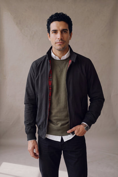 Medio cuerpo de la chaqueta Harrington negra de Luck & Load en capas sobre buzo verde oliva y camisa blanca.