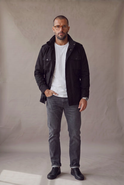 Hombre con chaqueta militar negra Luck and Load abierta sobre camiseta blanca, jean gris y tenis, de frente