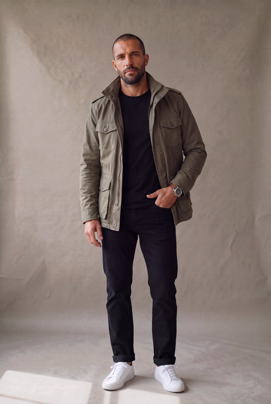 Chaqueta militar tipo M65 verde oliva para hombre de Luck and Load, abierta con cuello alto, sobre camiseta negra y jean negro recto; look casual premium de cuerpo entero.
