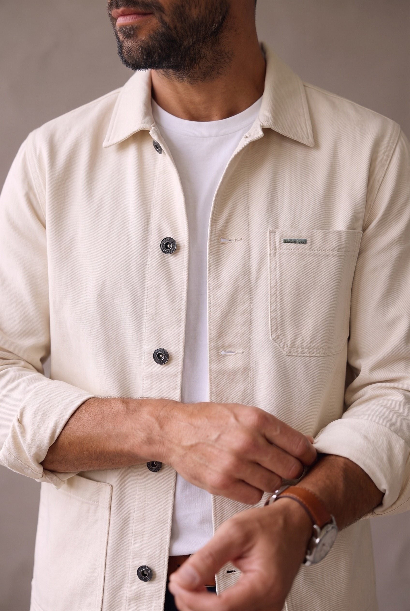 Detalle de la chaqueta obrera beige de Luck & Load: bolsillo de pecho con placa metálica, botones de peltre y ojales horizontales.