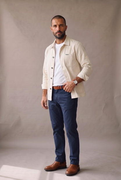 Chaqueta obrera beige para hombre de Luck & Load, look completo con camiseta blanca, pantalón azul marino, cinturón coñac y botines de cuero.