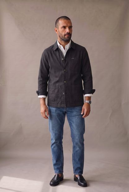 Chaqueta obrera negra para hombre de Luck & Load, vista frontal con la prenda abotonada sobre camisa oxford blanca.