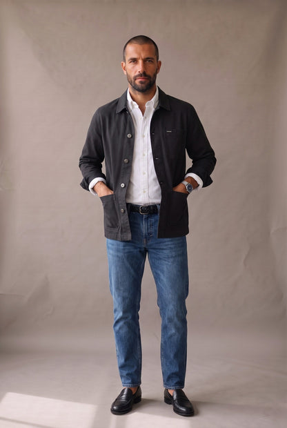 Chaqueta obrera negra para hombre de Luck & Load, vista frontal de cuerpo entero, abierta sobre camisa oxford blanca y jean azul.