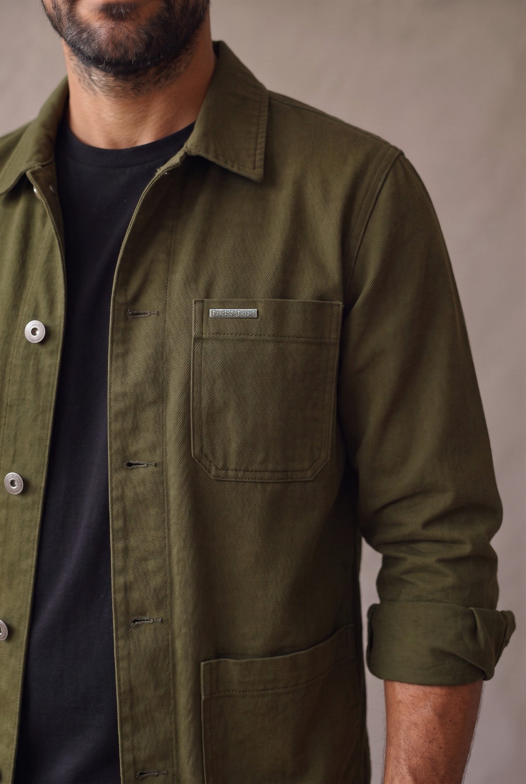 Detalle de la chaqueta obrera verde militar de Luck & Load: bolsillo de pecho con placa metálica grabada, botones de peltre y sarga de algodón en diagonal.